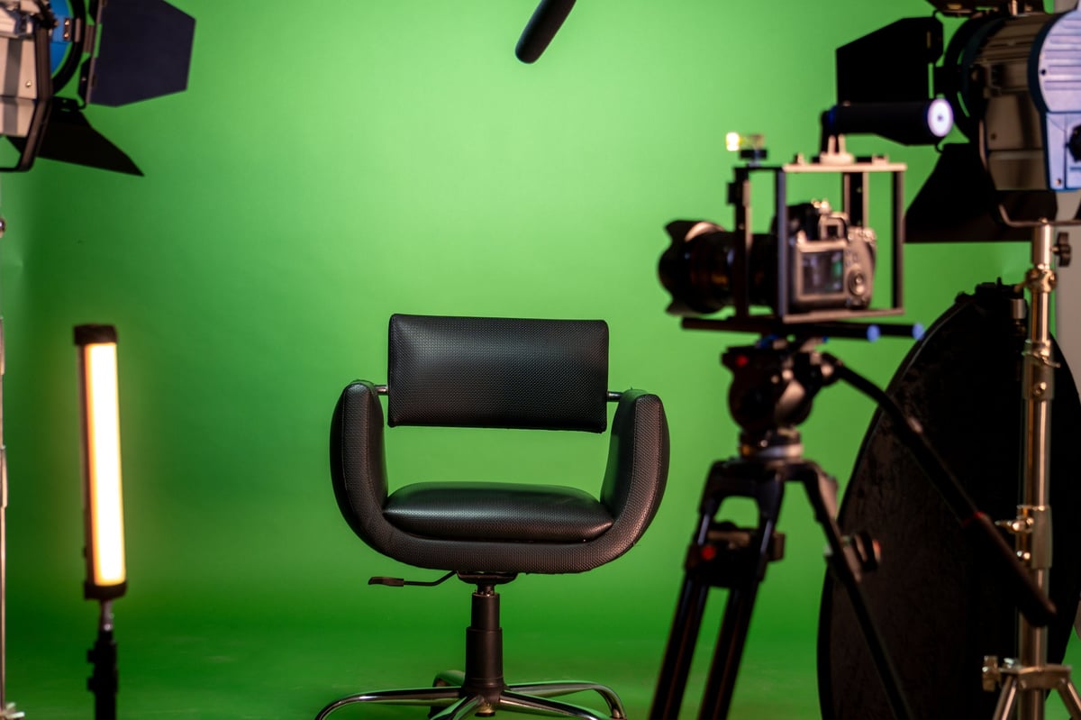 A fully equipped professional video studio with a green screen, camera, chair, and softbox lighting for content production